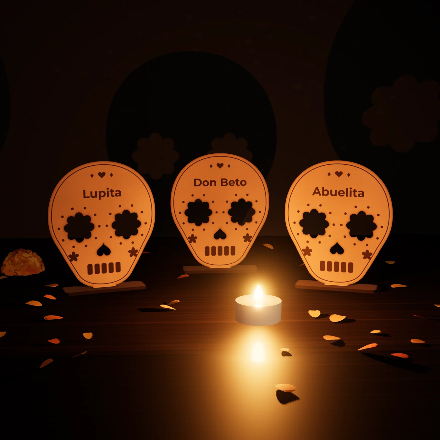 Tres calaveritas de MDF paradas en su base, con los nombres Lupita, Don Beto y Abuelita grabados en la frente, junto a una vela LED y pétalos de cempasúchil.