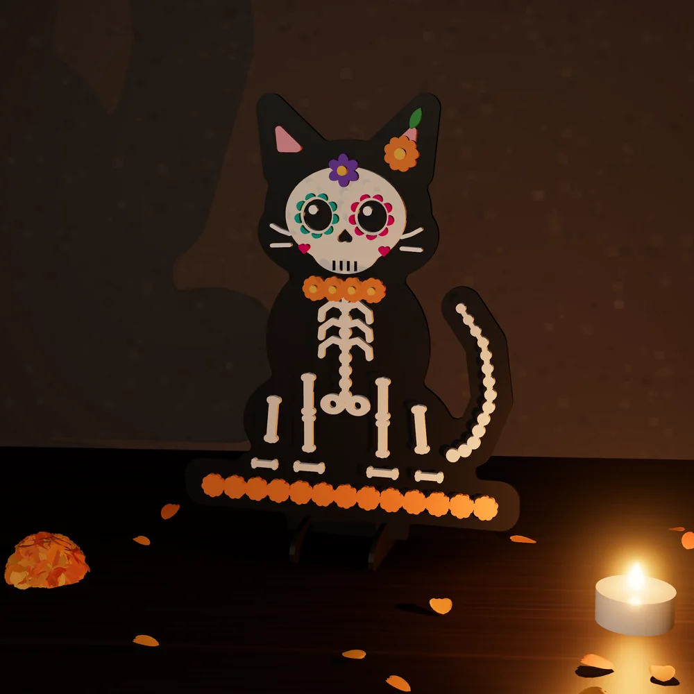 Gatito calavera de colores: figura de MDF en 4 capas pintadas, parada en su base junto a una vela y pétalos de cempasúchil.
